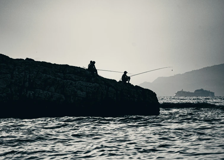 people are fishing off a rocky edge above the water