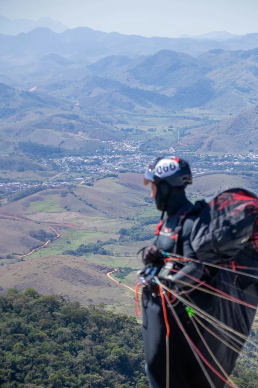 a man with a helmet and rope on his back holds onto some type of wind sail on top of a mountain