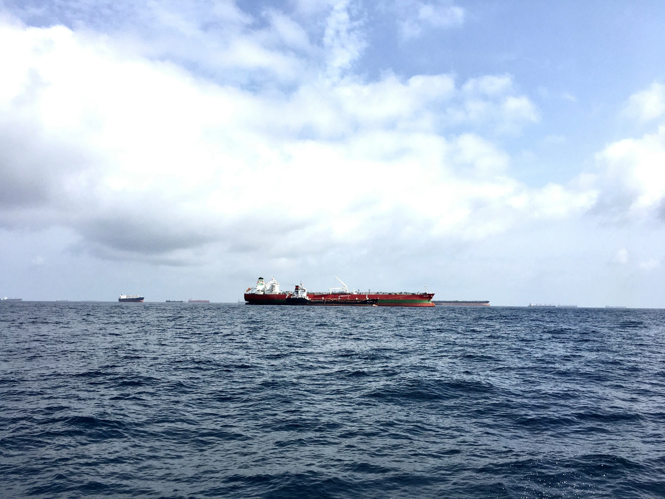 two boats sailing in the ocean with a boat and a cargo ship behind