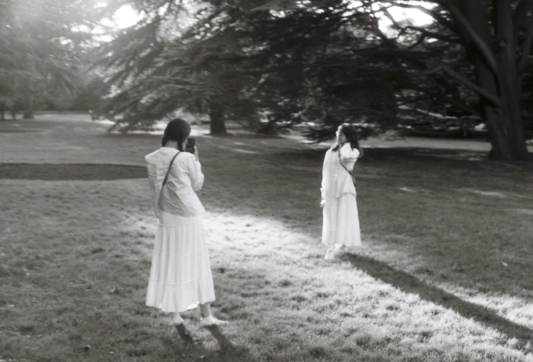 two women in long dresses stand near trees