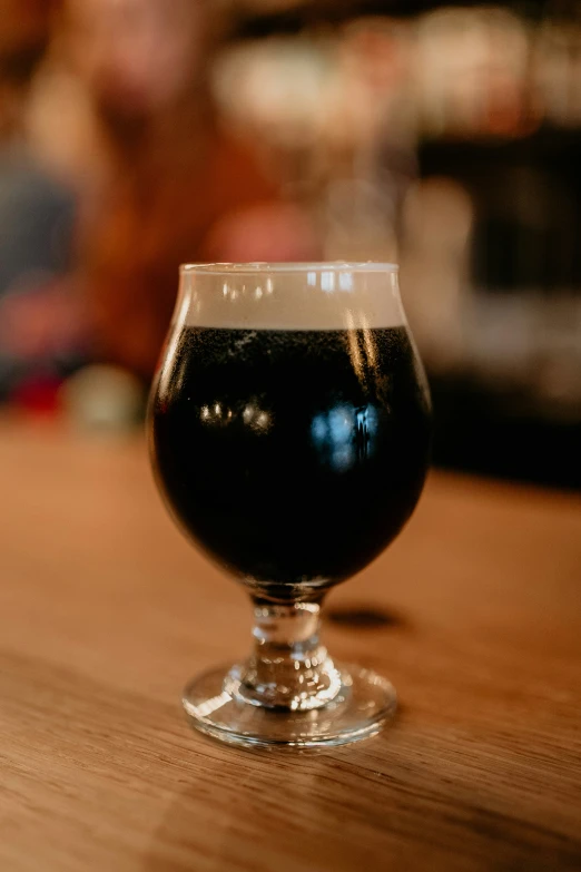 a glass filled with dark beer sitting on a table