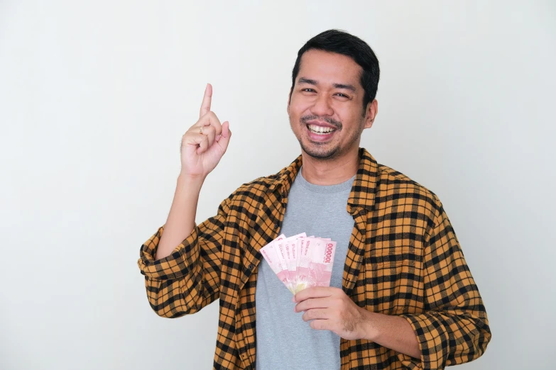 a man pointing up while holding onto a pair of pinky cash