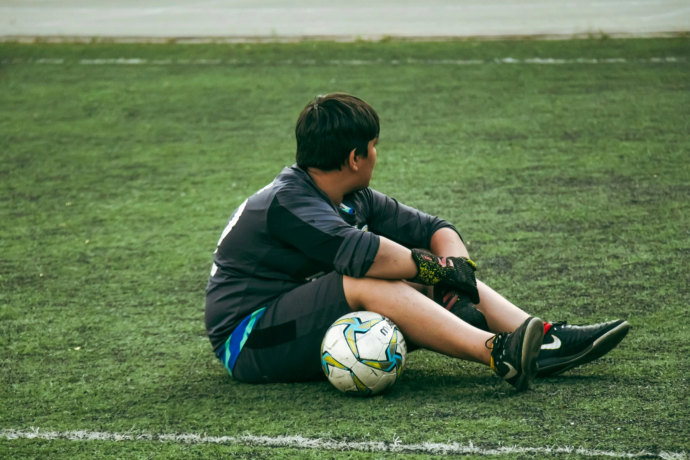 a boy sitting on the ground in front of a soccer ball