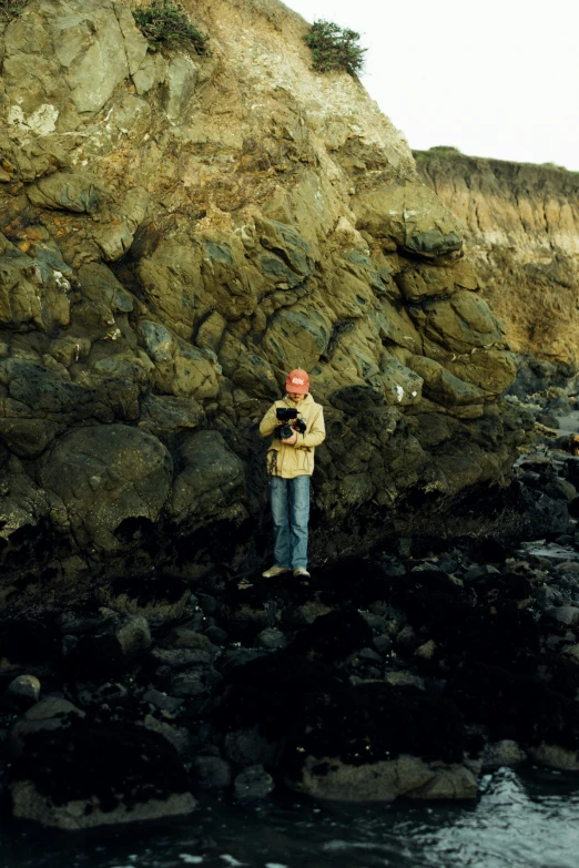 a man in a tan jacket standing on rocks and water