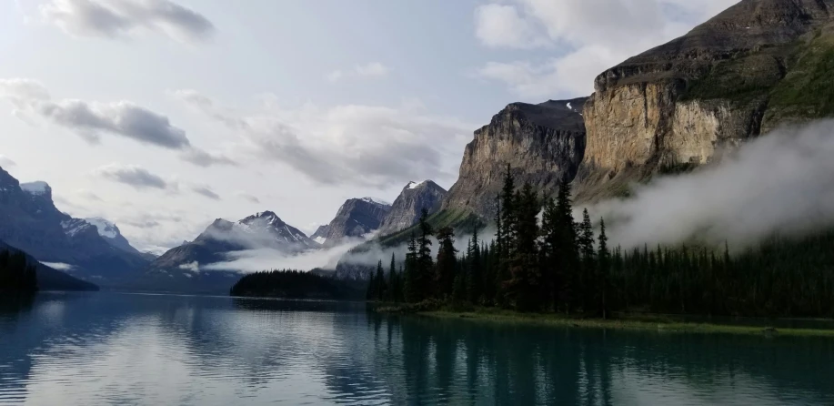 clouds float across the water on top of the mountains