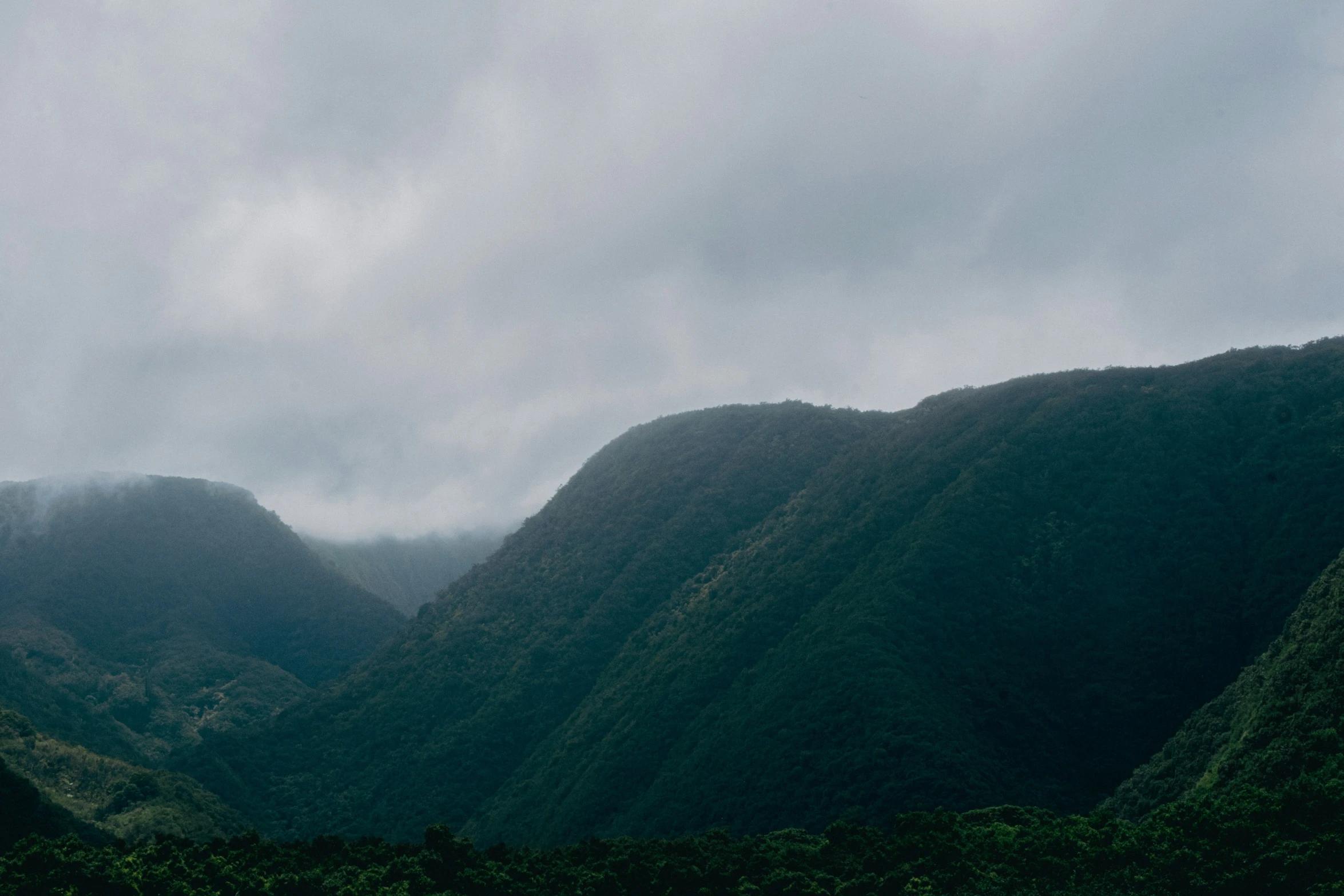 an overcast sky is shining on the tops of mountain peaks