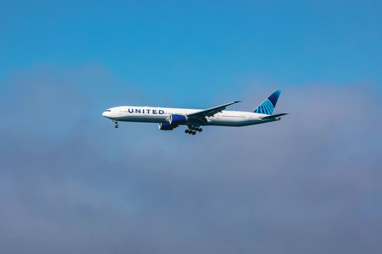 a blue and white airplane flying through a cloud filled sky