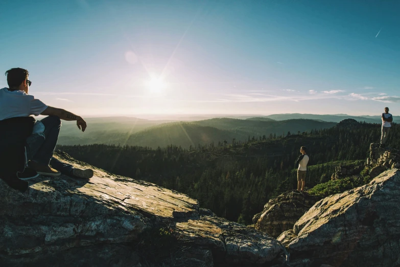 a man sitting on the side of a mountain as another man watches