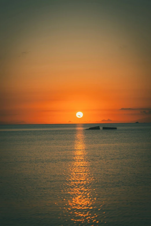 sunset over the ocean with two small boats in front of them