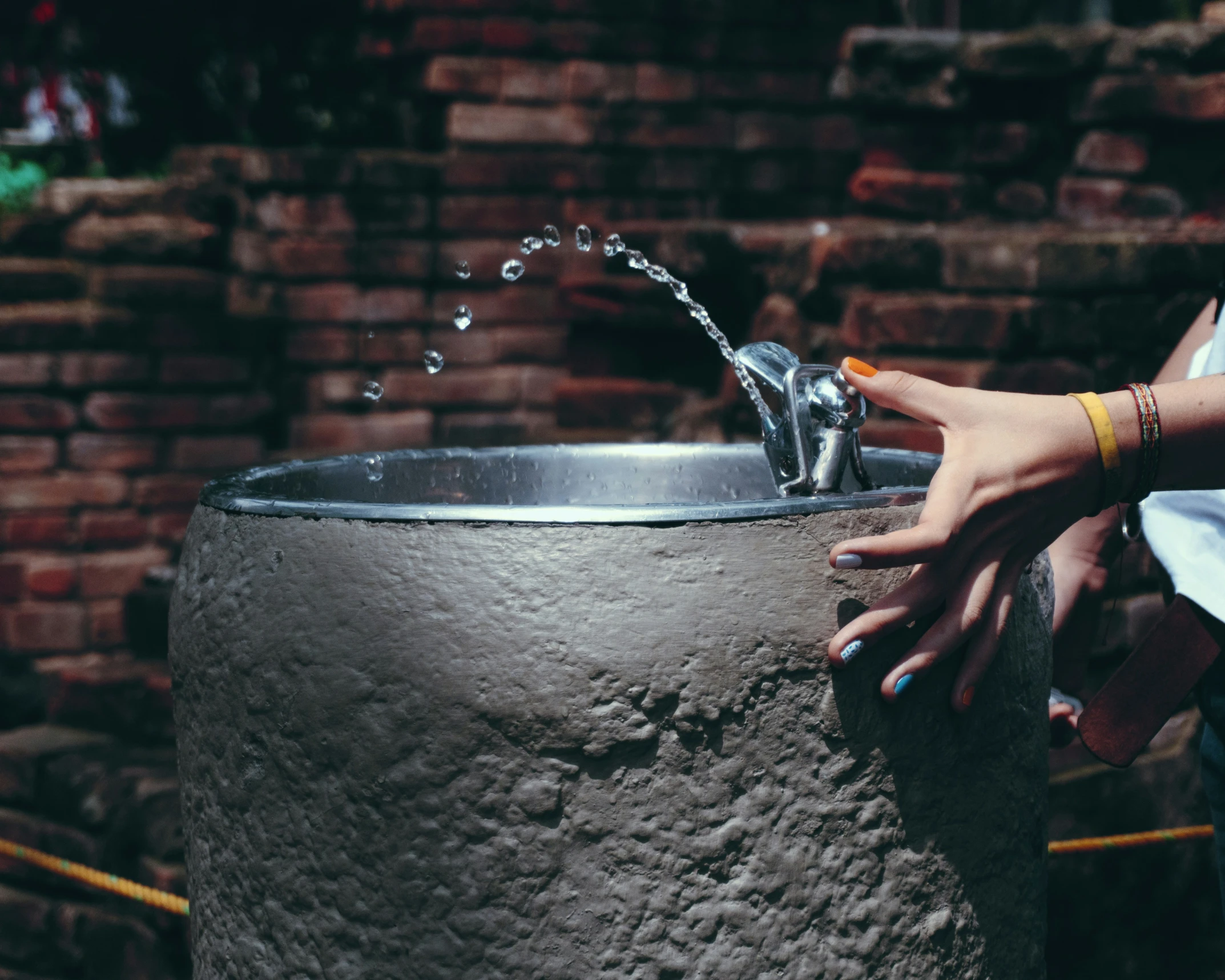 person's hand holding onto water hose in large grey pot