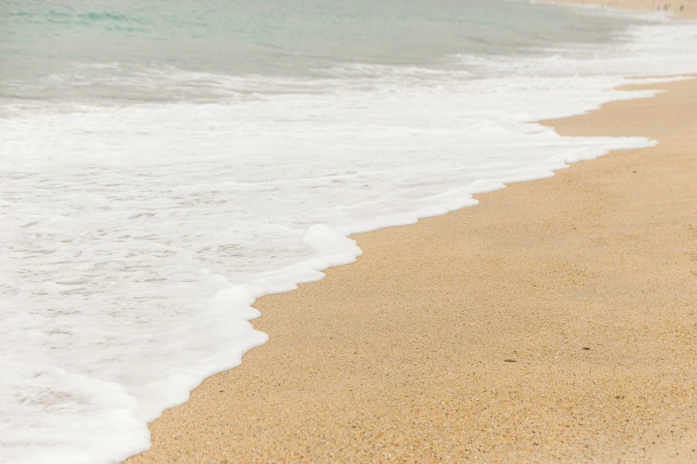 water lapping on the shore with a surf board leaning against it