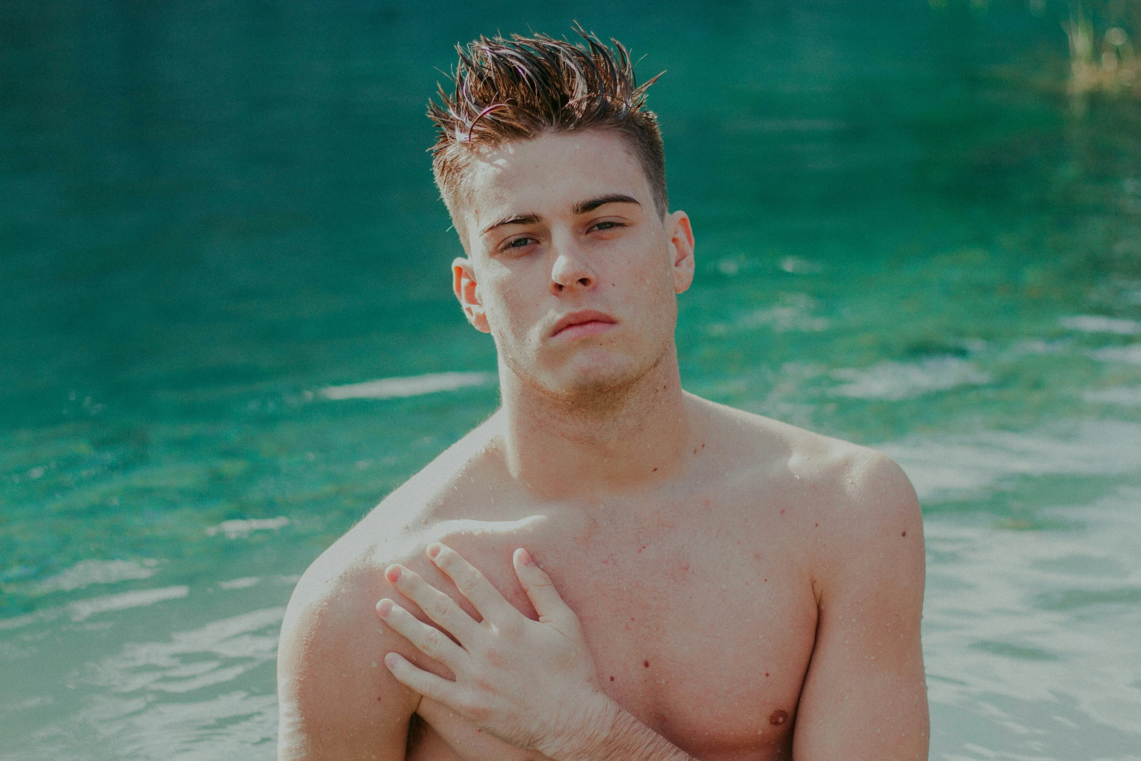 young man standing in clear water near green trees