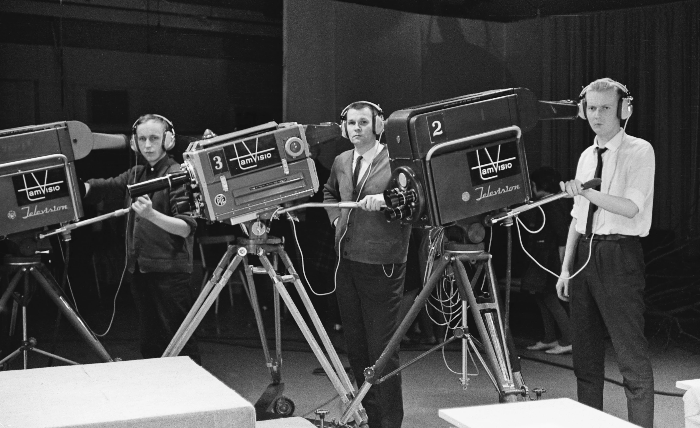 four men stand with headphones on in front of camera