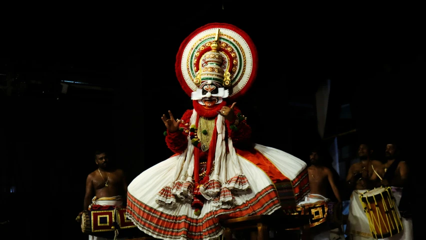 a man dressed in white and red poses with some drums