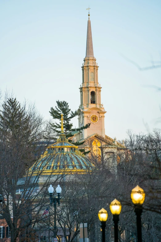 tall church steeple rises in the background while lit street lamps are nearby