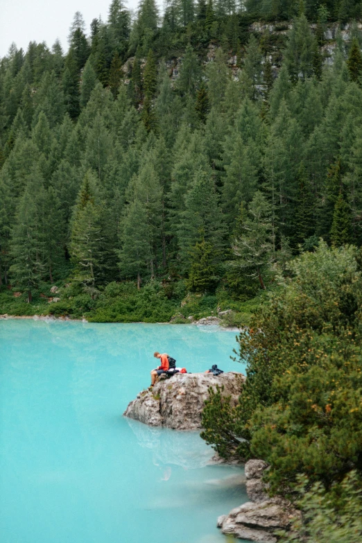 there are several people sitting on the rocks by a lake