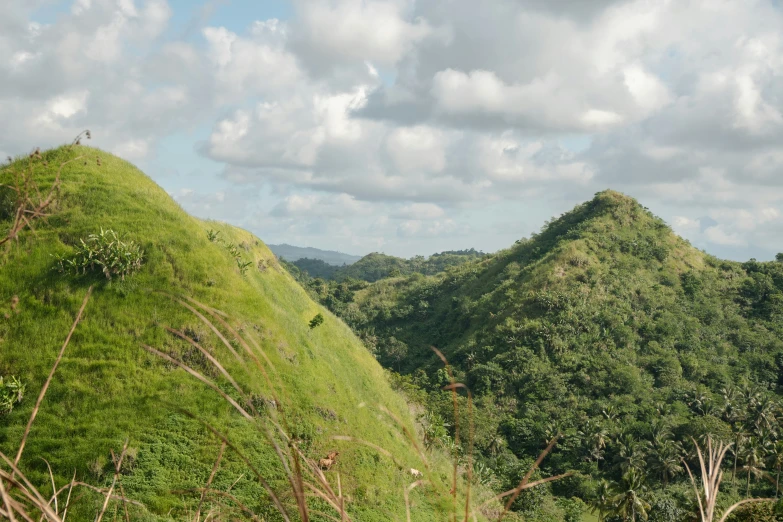 two green mountains covered in vegetation under a cloudy sky