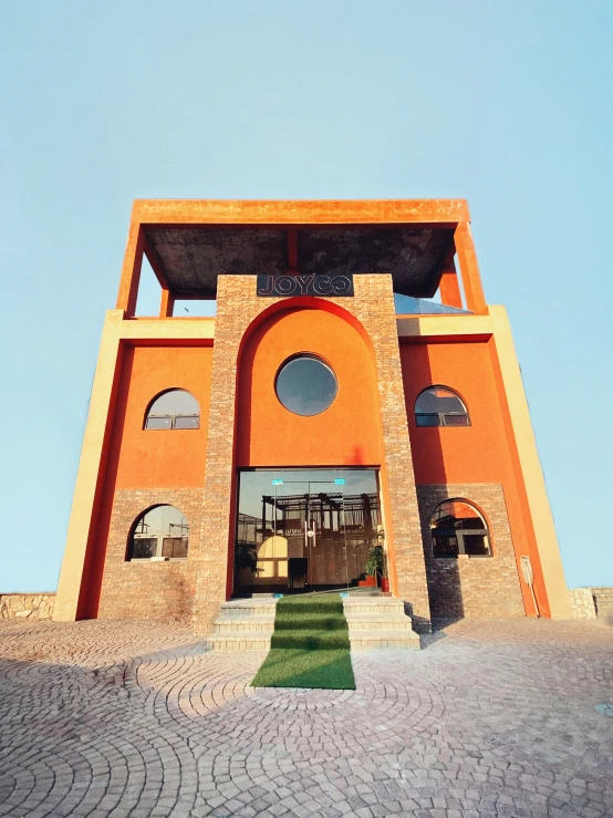 a red, round - shaped building with a green lawn and stairs leading up to it