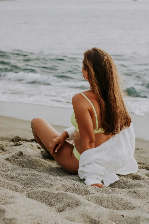 a woman sits on the beach in a bikini top