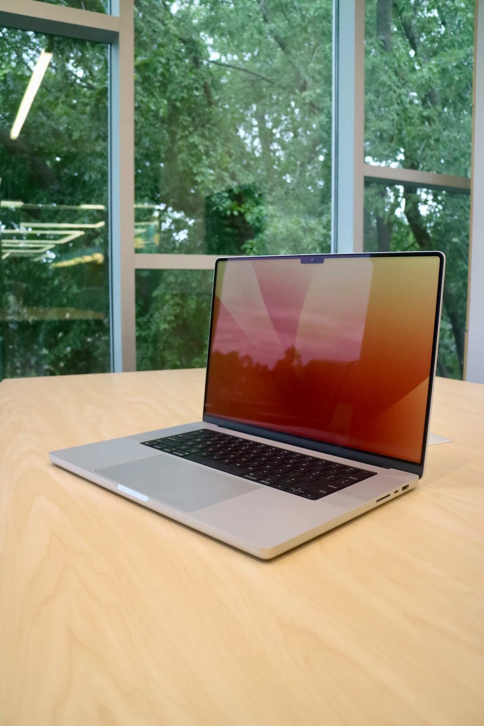 the laptop sits on a wooden table near a window