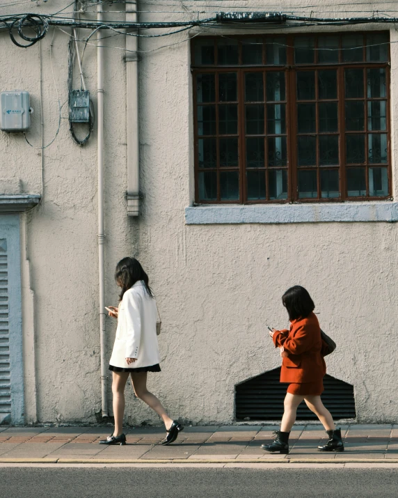 two people walk down a sidewalk next to a building