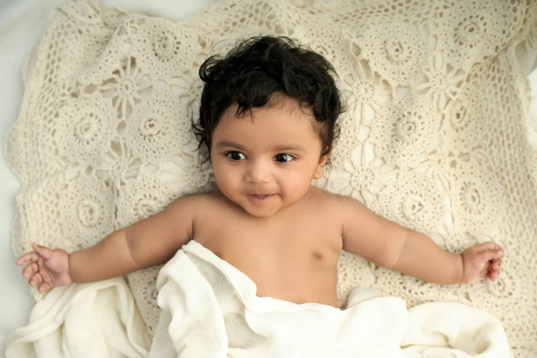 an adorable young baby smiles as it lays on a blanket