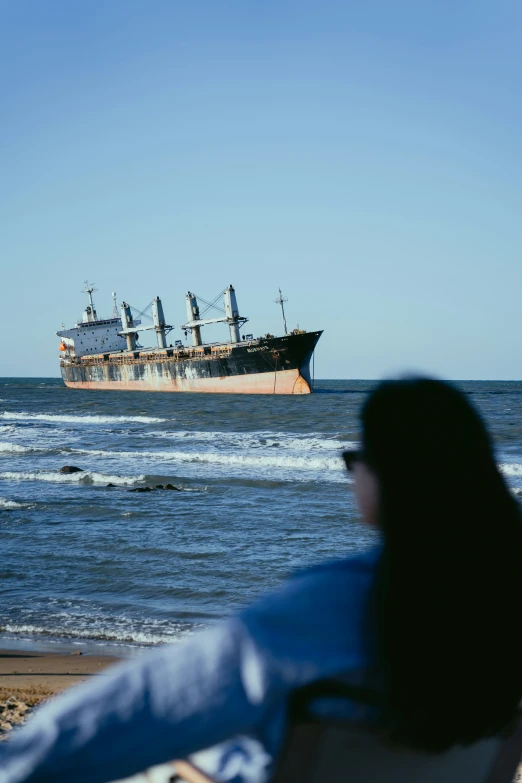 the woman is sitting in a beach chair looking at a ship