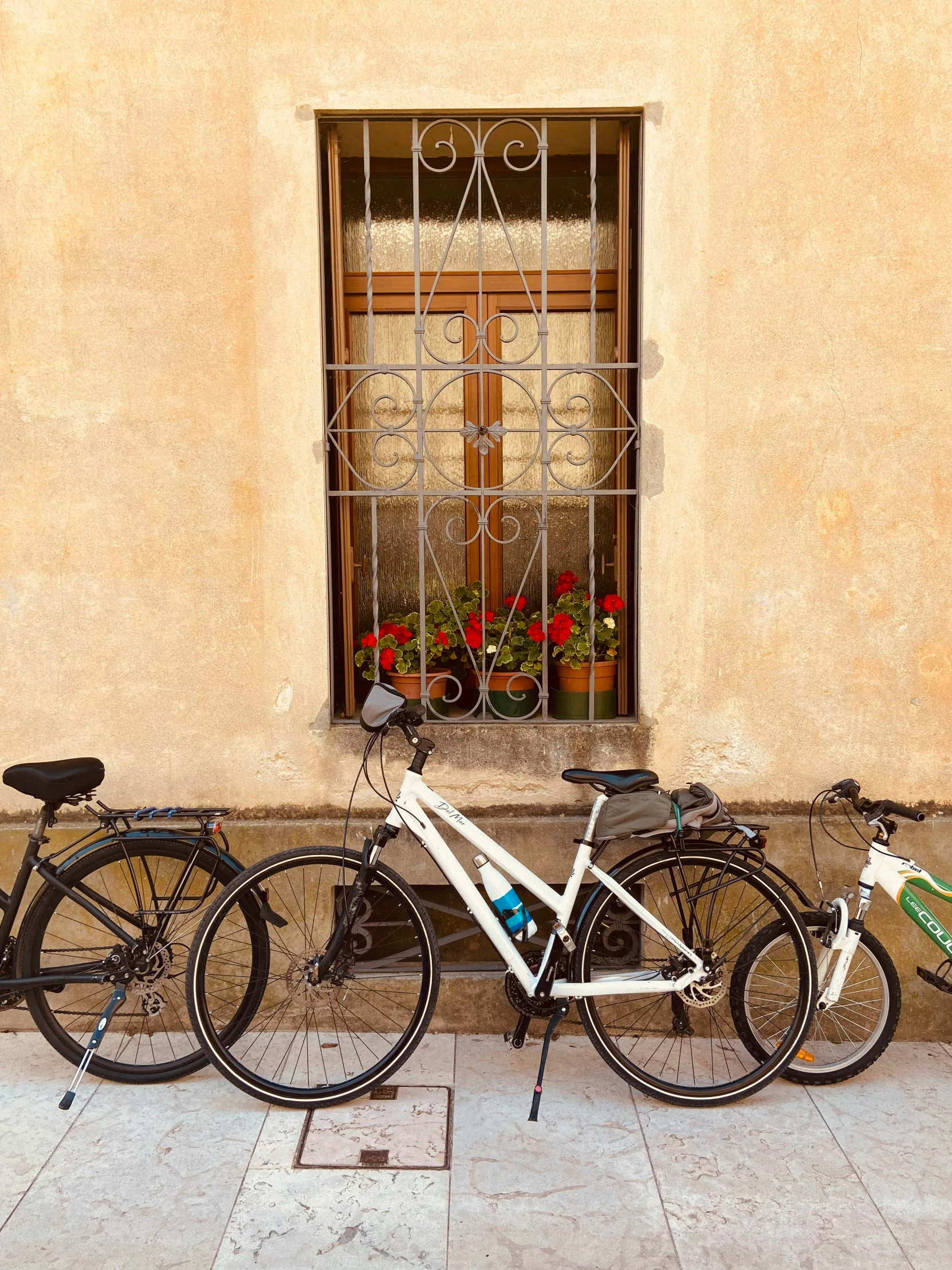 two bikes parked in front of a window near a tile sidewalk