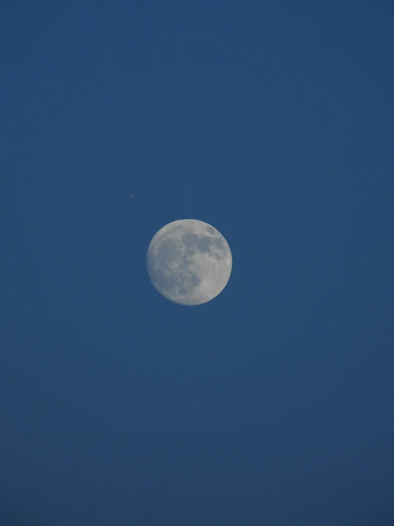 the moon with a jet flying past in a blue sky