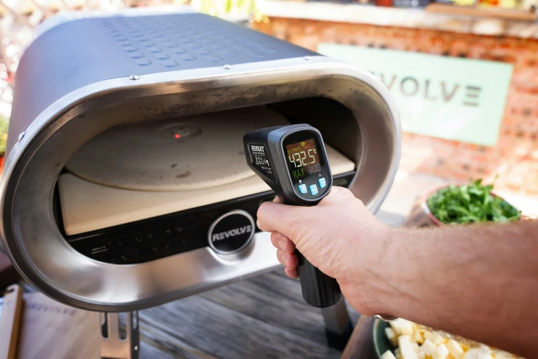 someone using a device to examine a pizza on a grill