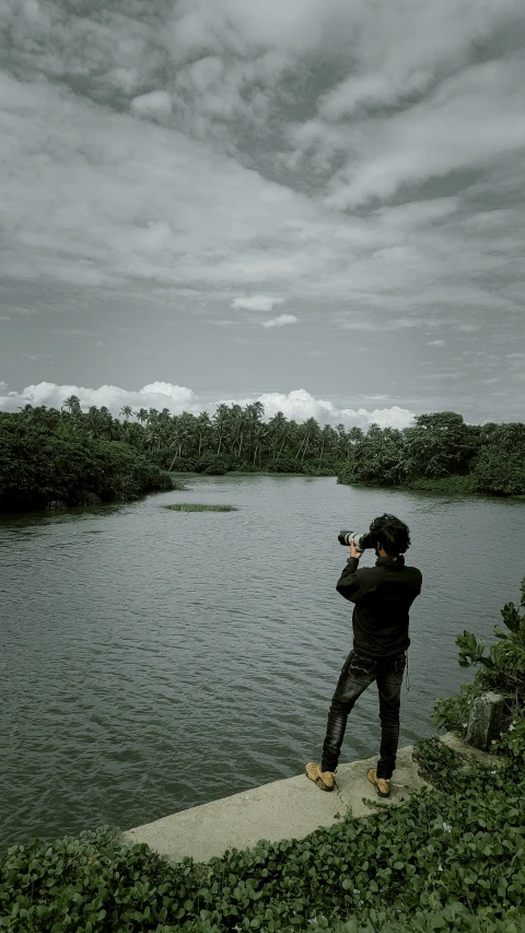 a man standing next to a river on top of a lush green field