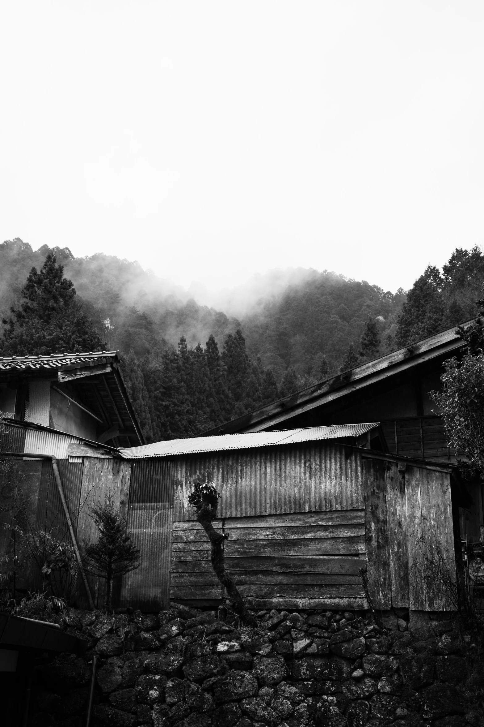 the mountains are very dark and foggy as people stand near a barn