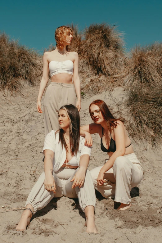 a trio of young women in white attire standing on a beach