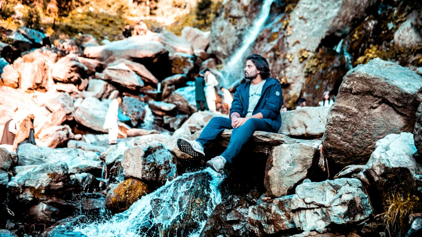 a man sits on some rocks near water