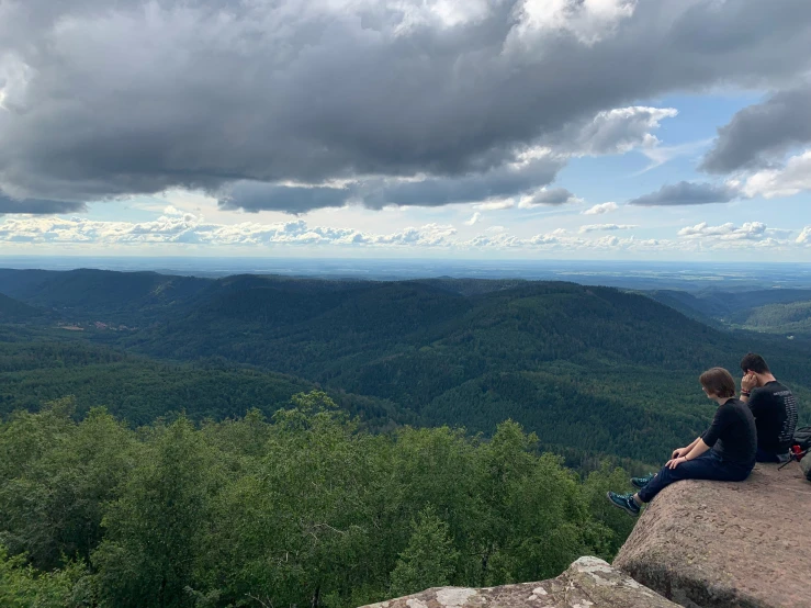 two young people sit on top of a rock near the forest