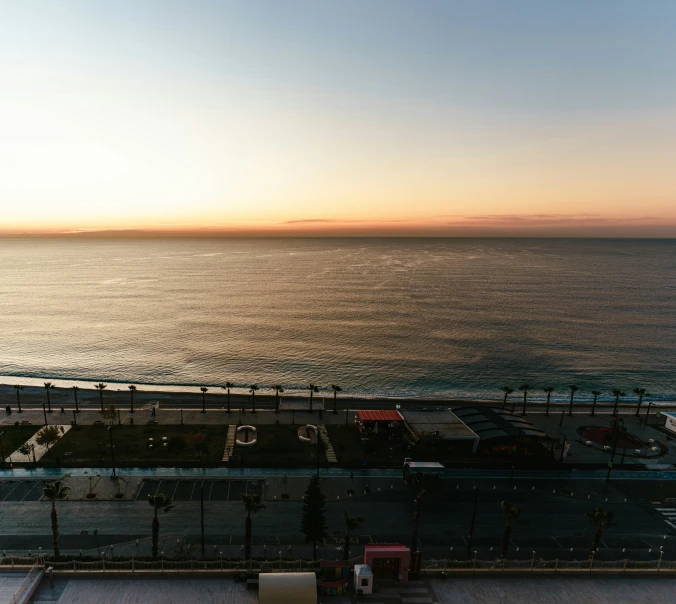 a long highway next to the ocean with the sun setting in the sky