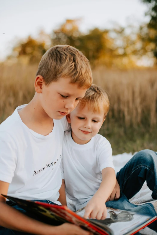 a little boy and his younger brother sit in a field together