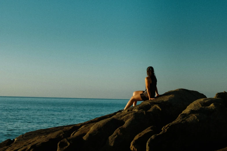 a girl is sitting on some rocks near the ocean