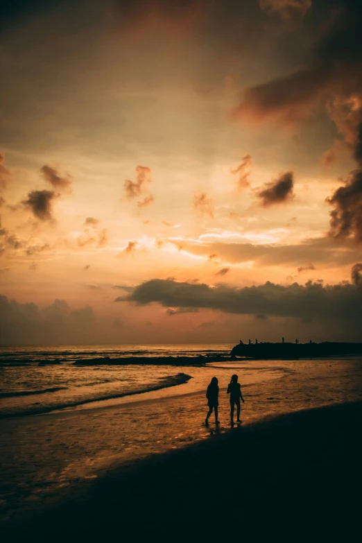 two people standing on a beach watching the sunset