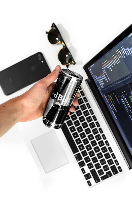 a person is holding a beer in front of a laptop