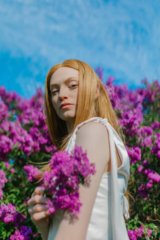 a girl with red hair is standing by flowers