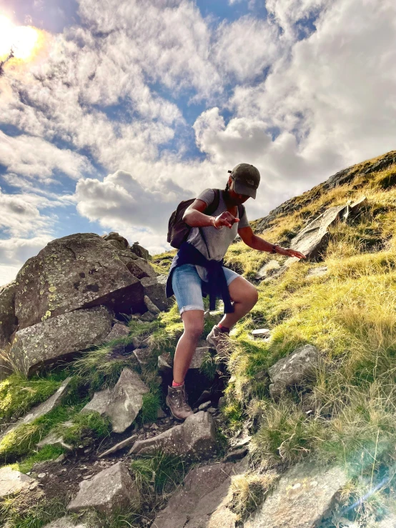 a man climbing up a steep, grassy hill in the mountains