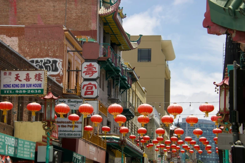 rows of chinese style lanterns with oriental writing and red paper lantern lights are suspended above the street