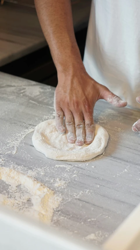 a person kneading a ball of dough on top of a counter
