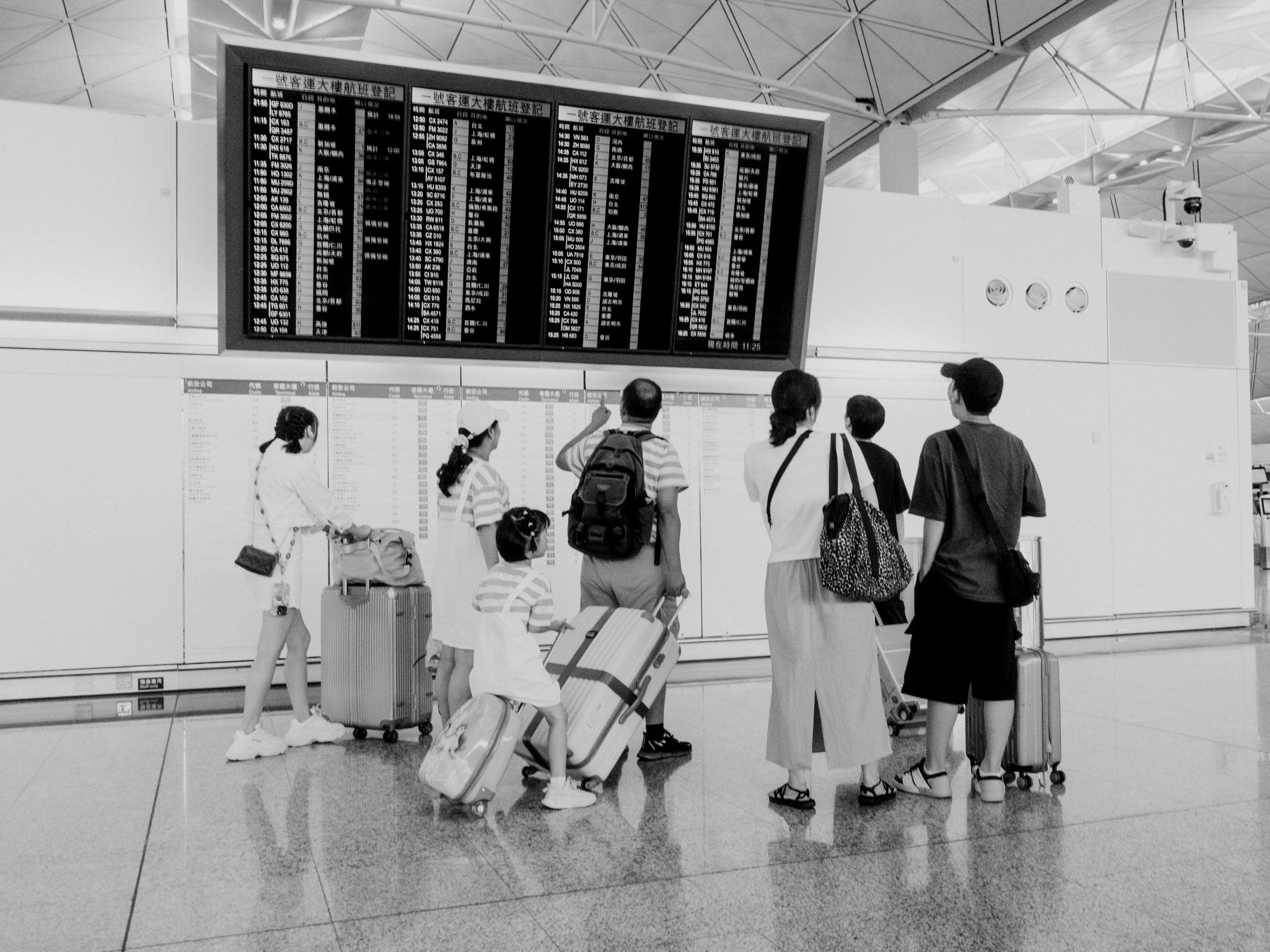 three people waiting for their luggage in front of a timetable