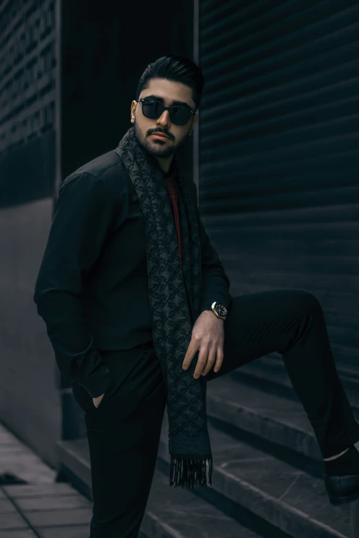 a man in sunglasses and a scarf leaning on a wall