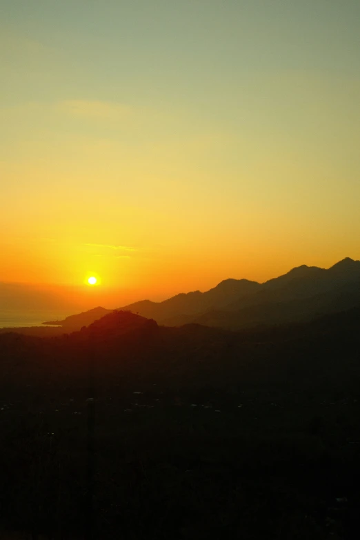 a view of the sun setting over mountains with a kite