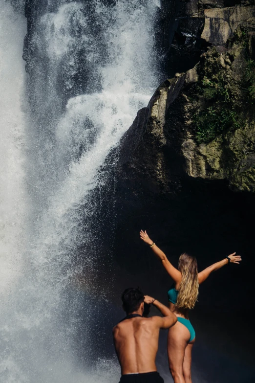 there is a woman standing in front of a water fall with her arms raised