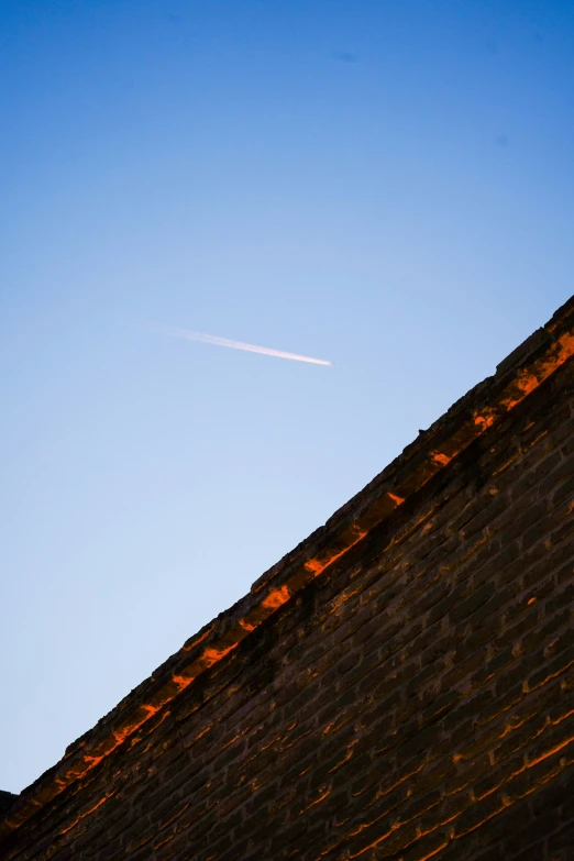 the sky above the brick building has an aeroplane contrail