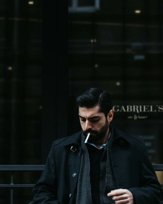 a man wearing a coat smoking and holding a cigarette